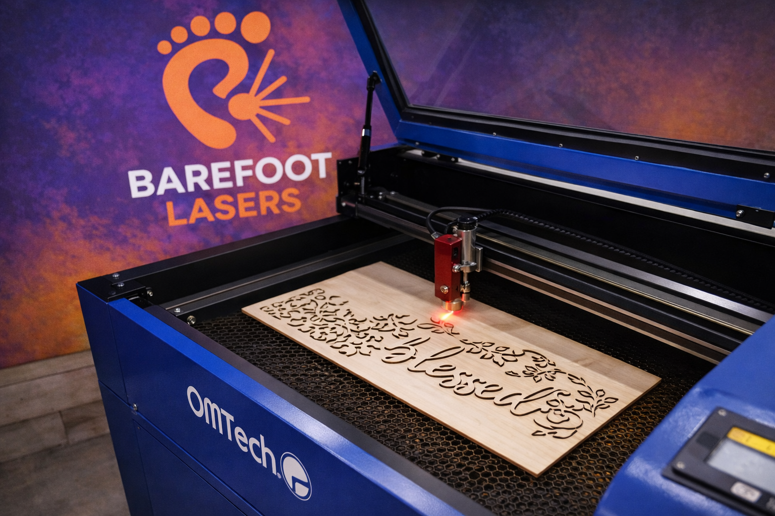 Blue OMTech laser cutter engraving a maple wood sign in the Barefoot Lasers workshop.